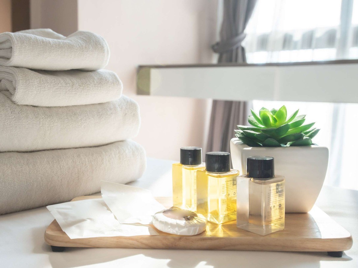 Guest amenity miniatures on a wooden tray beside folded towels and a succulent