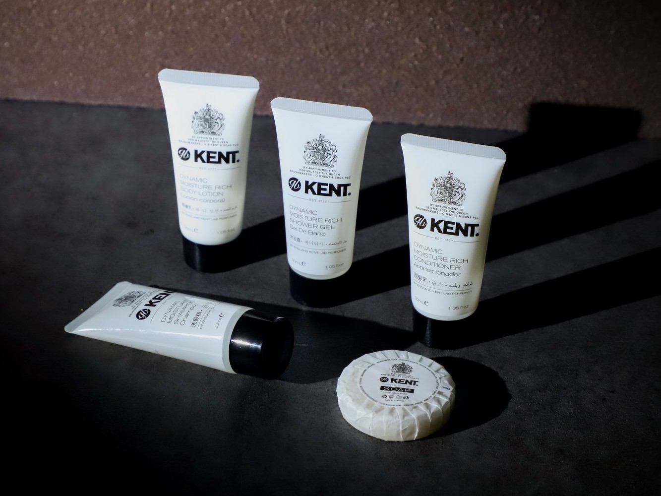 Kent hotel amenity tubes and a wrapped soap on a dark surface