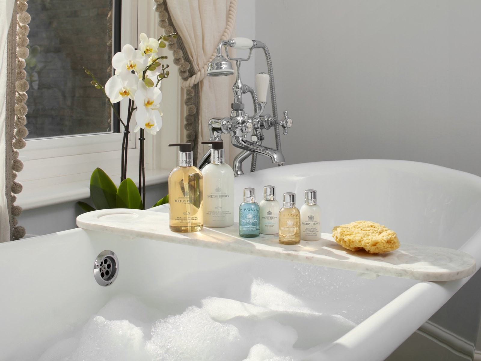 Molton Brown amenities on a marble caddy across a roll-top bath