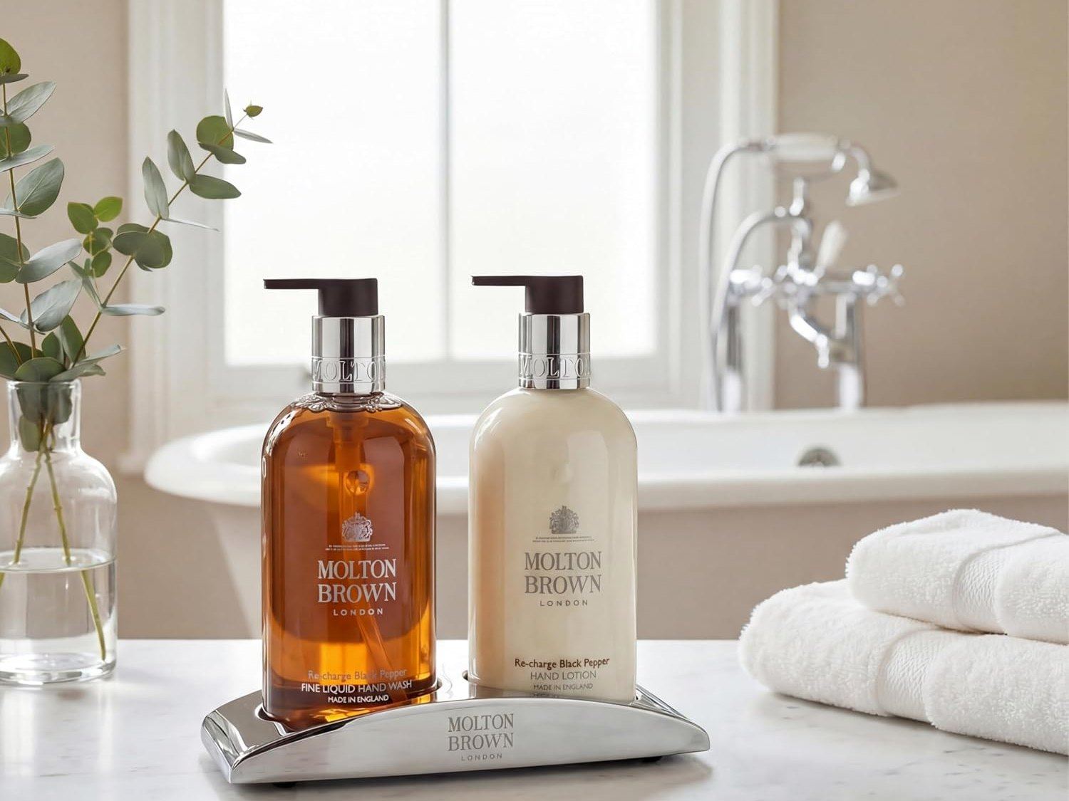 Molton Brown glass hand wash and hand lotion on a chrome tray beside a marble bathroom counter