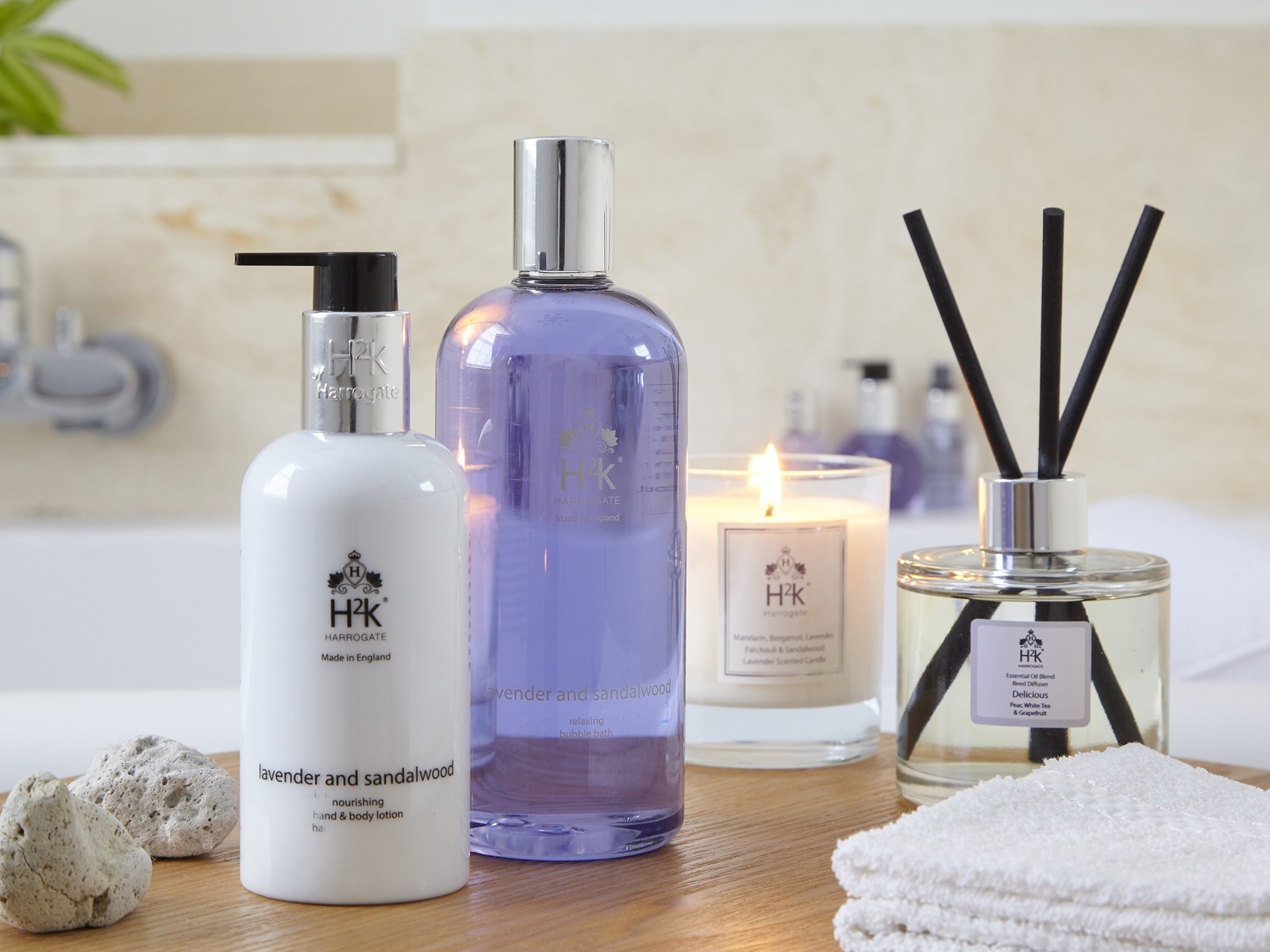 H2K Lavender and Sandalwood hand and body lotion and bubble bath beside a scented candle and a reed diffuser