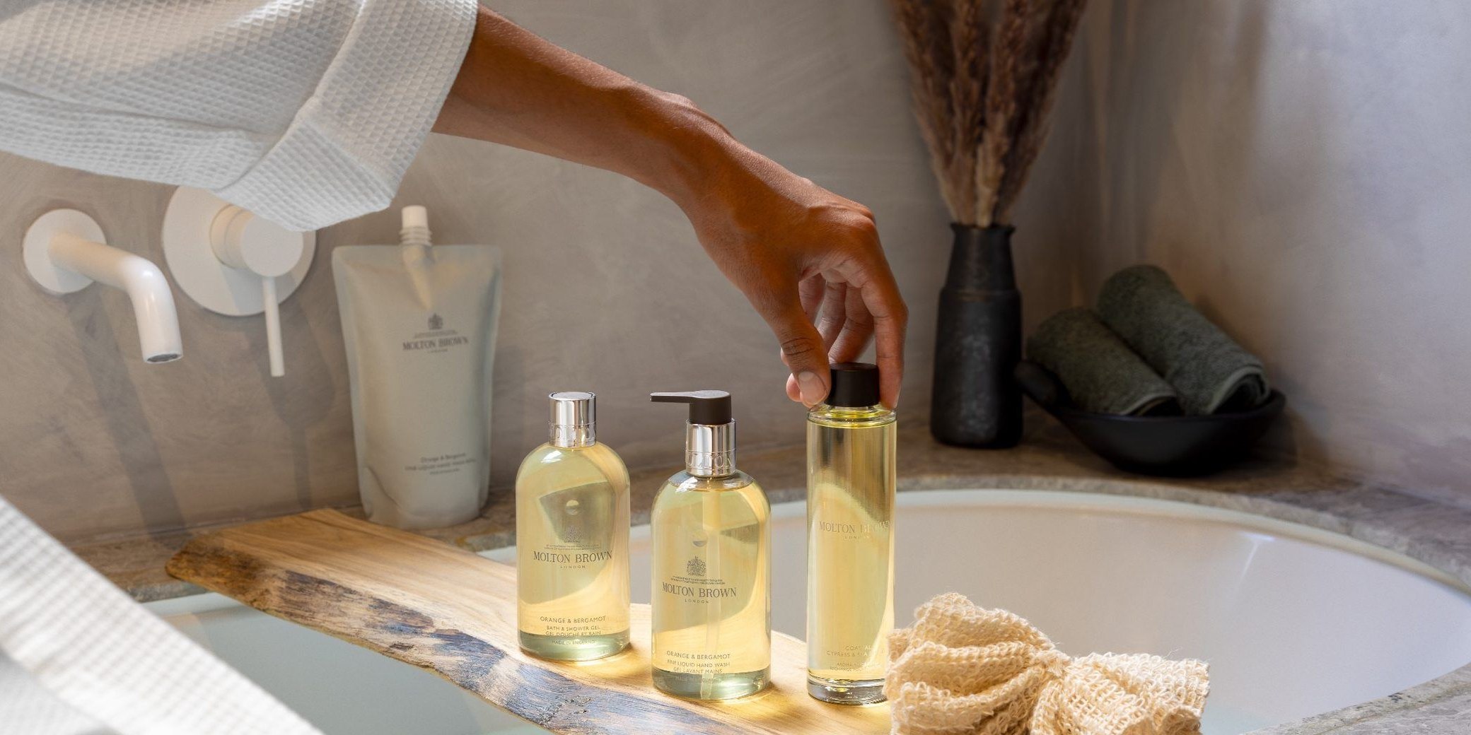 Molton Brown Orange & Bergamot bottles and a refill pouch on a timber bath caddy in a hotel bathroom