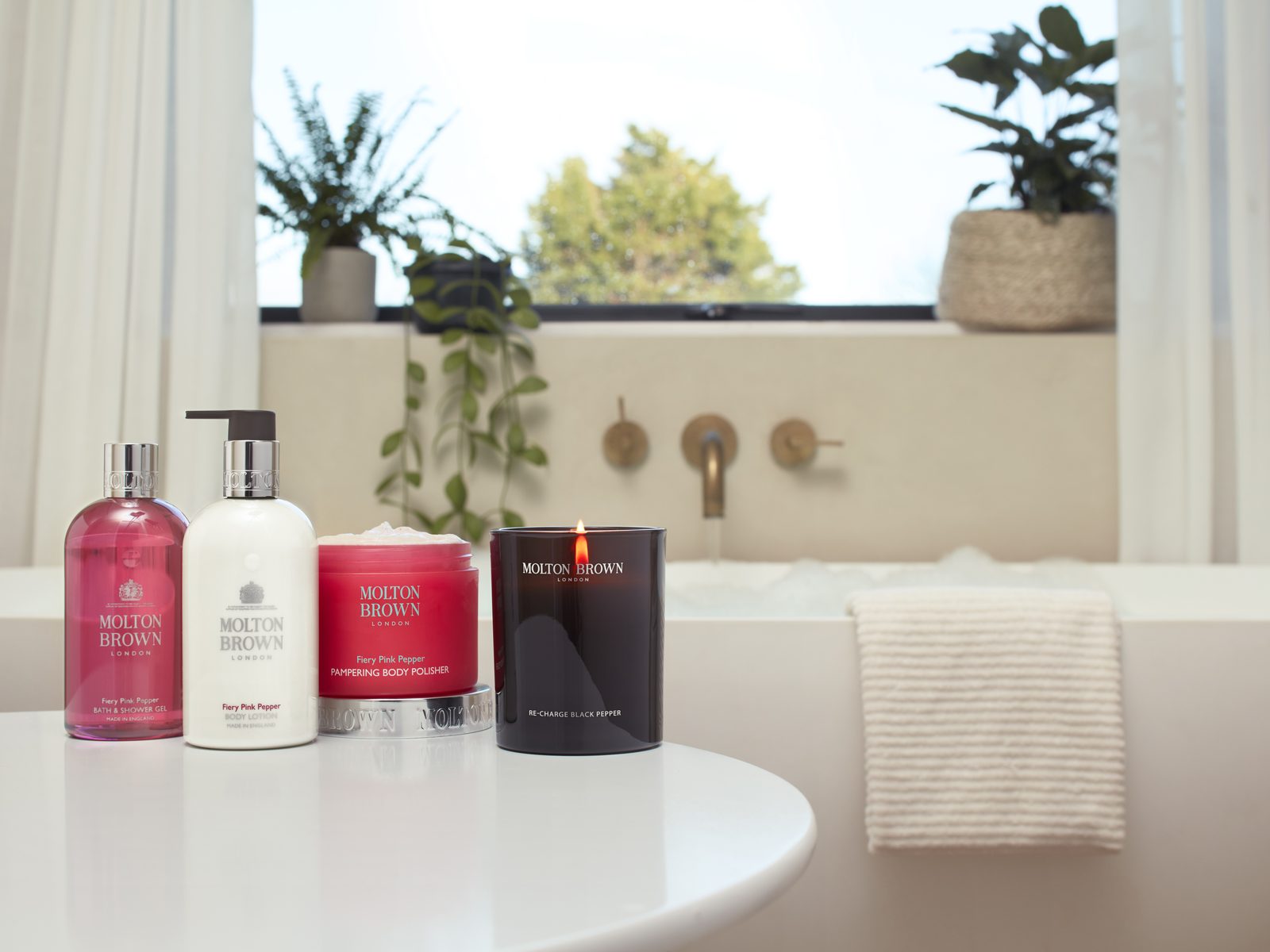 Molton Brown Luxury collection beside a hotel bathtub with bronze fittings and garden view