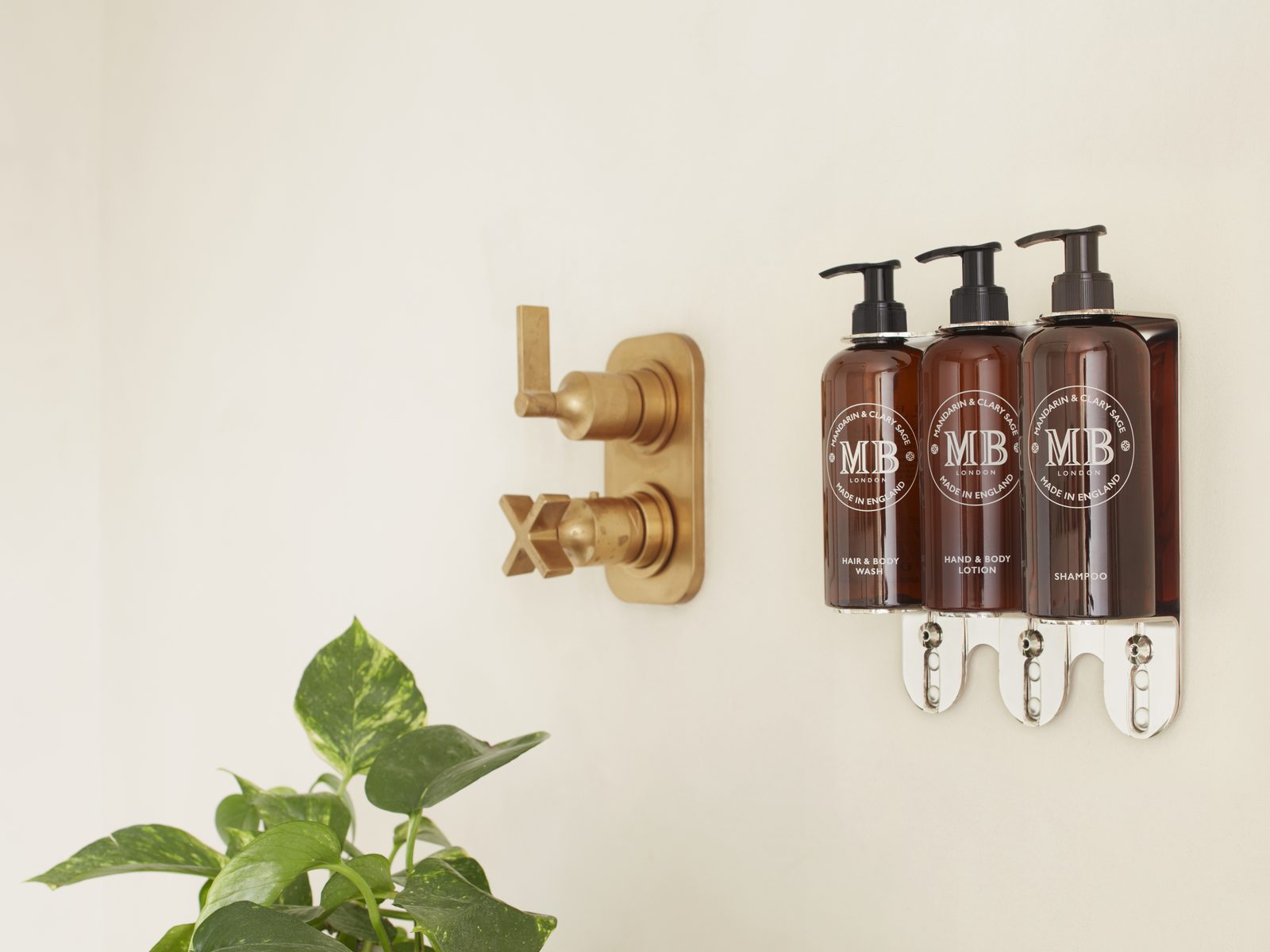 Molton Brown dispensers on a bronze wall bracket beside a brass shower mixer