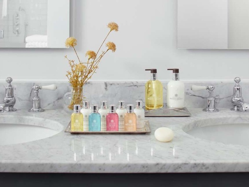 Molton Brown 300ml bottles and a tray of miniatures on a marble double vanity in a hotel bathroom