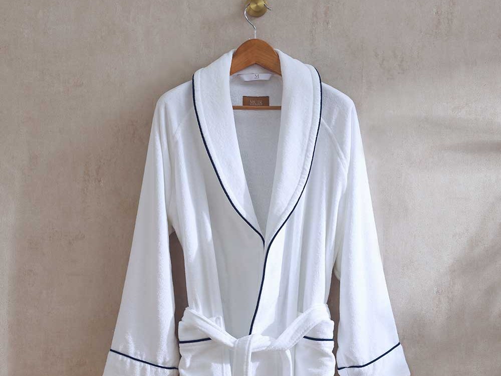A Muir Velour Empire bath robe in white with navy piping, hanging on a wooden hanger
