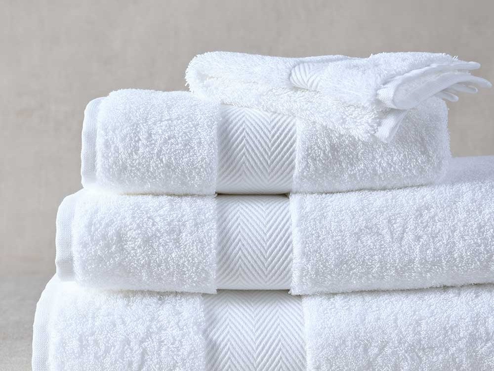 A stack of Muir Signature Supima cotton towels in white with a herringbone border, and face cloths