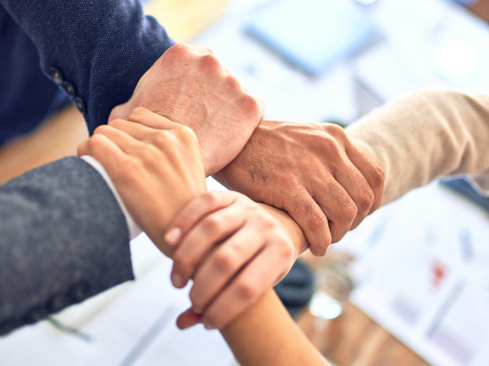 Four colleagues joining hands across a meeting table